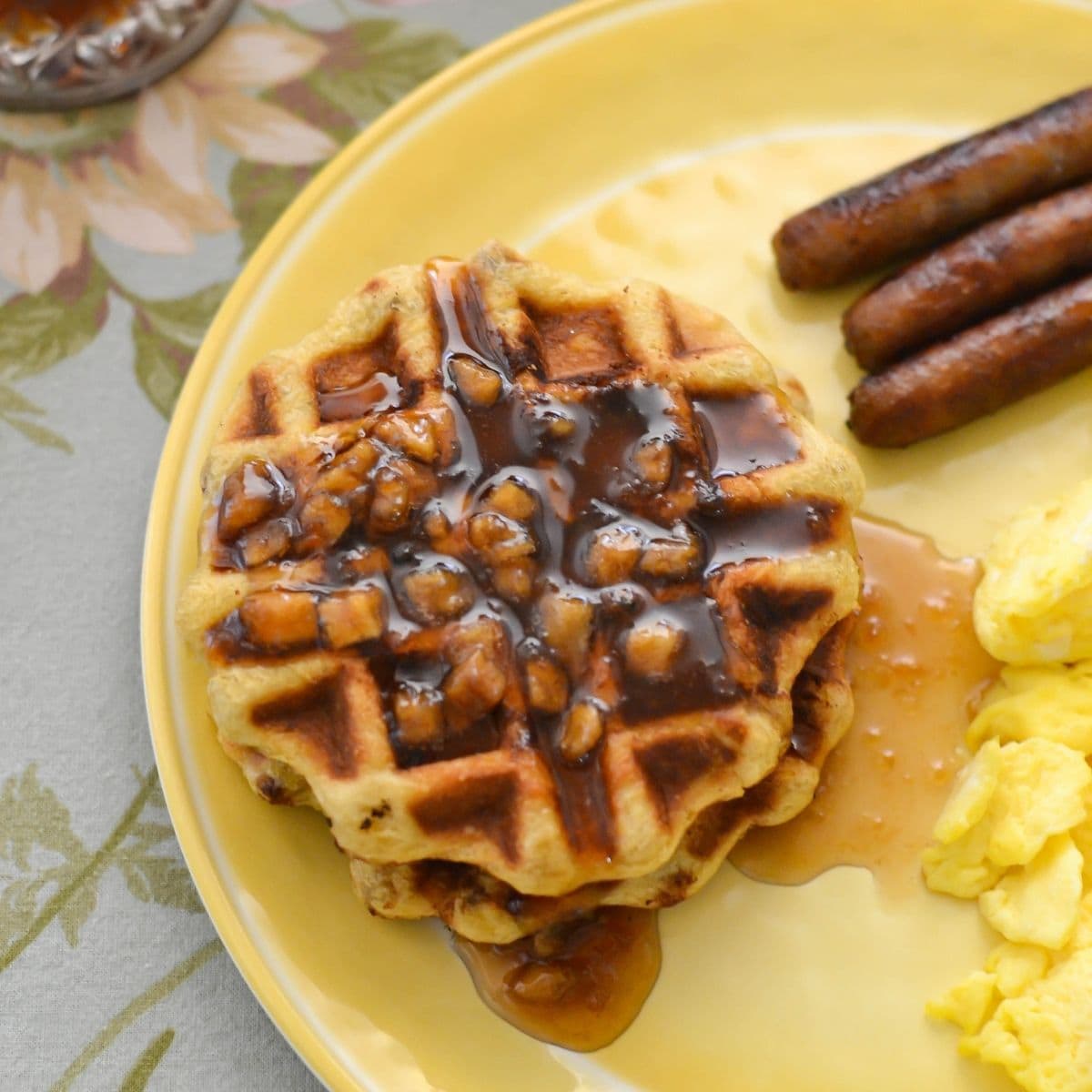 Apple Cinnamon Roll waffles on a plate with sausage links and scrambled eggs.