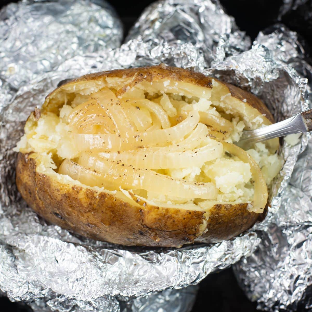 Overhead image of a baked potato cut open down the middle with sliced onion and melted butter.
