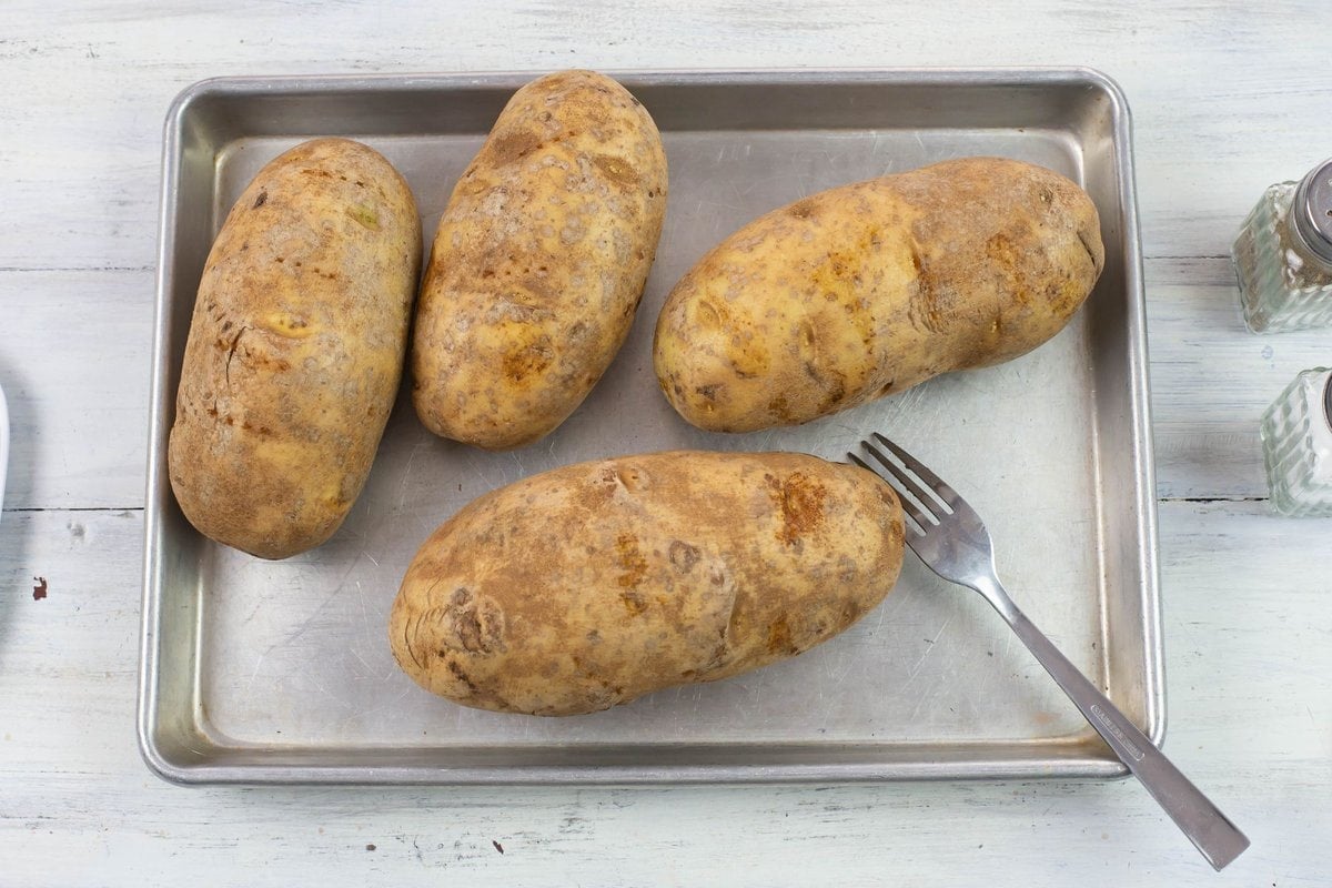4 large baking potatoes that have been poked with a fork on a baking sheet.
