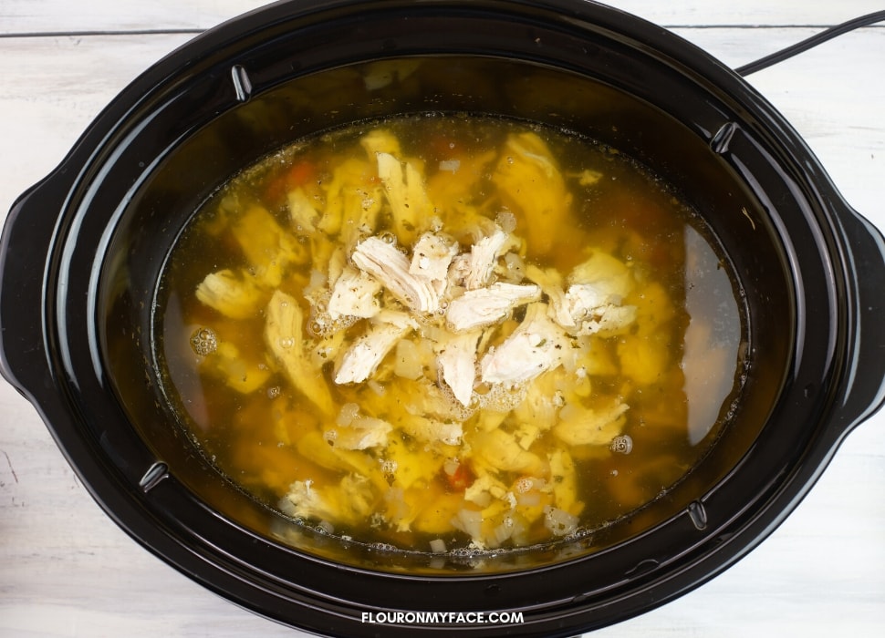 shredded chicken cooking in a crock pot with chicken broth