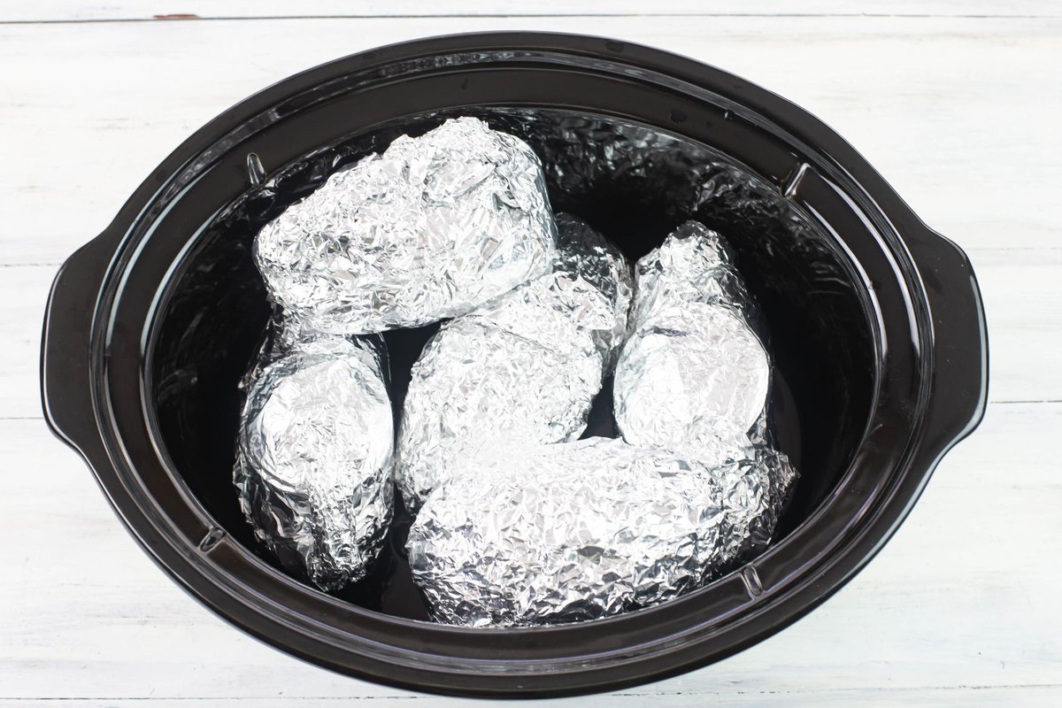 5 Potatoes wrapped in aluminum in a crock pot.