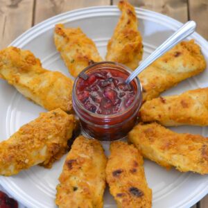 Sweet and spicy cranberry pepper dipping sauce in a small jar surrounded by chicken strips on a plate.