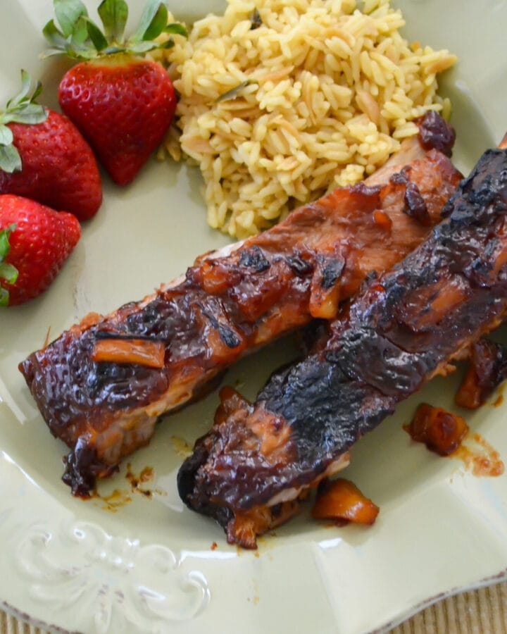 Hawaiian style BBQ Pork Ribs served on a green plate with fresh strawberries and yellow rice.