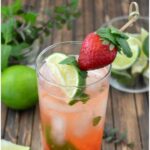 Strawberry Mojito served in a tall glass with berries, lime wedge and mint.