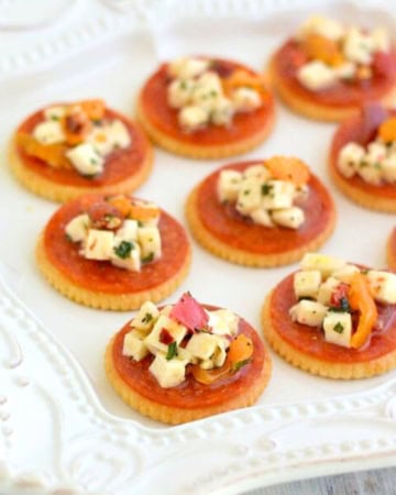 Pepperoni Bruschetta served on a cracker on a white plate.