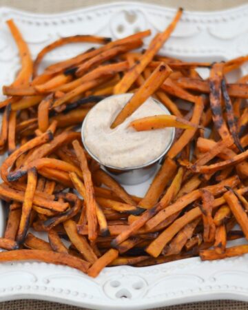 White dish with crispy sweet potatoe french fries and a bowl of dip.