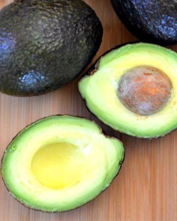 Whole & sliced avocados on a cutting board.