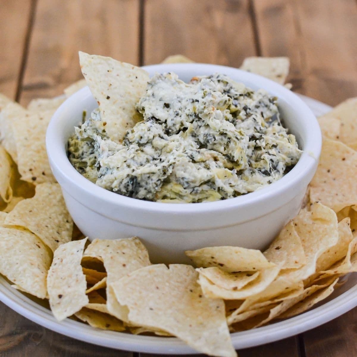 Hot artichoke and spinach dip served in a small bowl with chips.