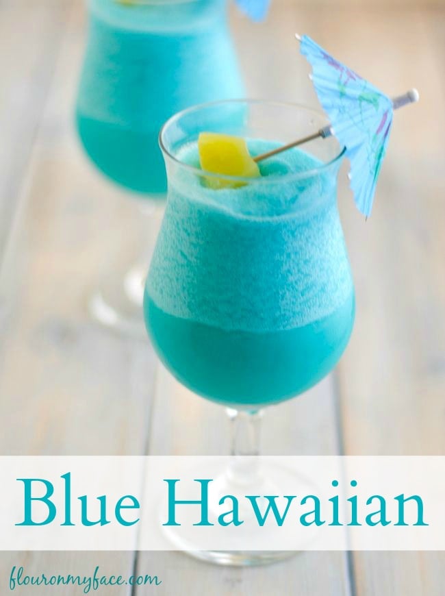 Frozen Blue Hawaiian Cocktail served in a hurricane glass with a blue paper umbrella and chunk of pineapple