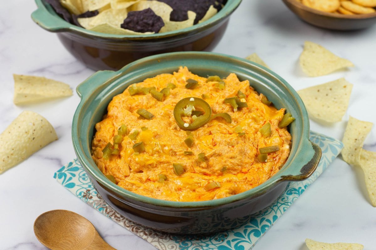 Buffalo chicken dip in a serving bowl with a bowl of tortilla chips in the background.