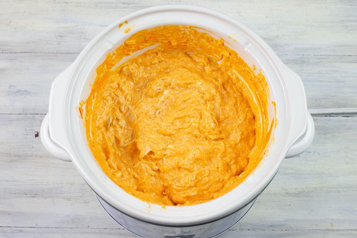 Buffalo chicken dip as it slow cooks and the cheeses are melting in a crock pot.