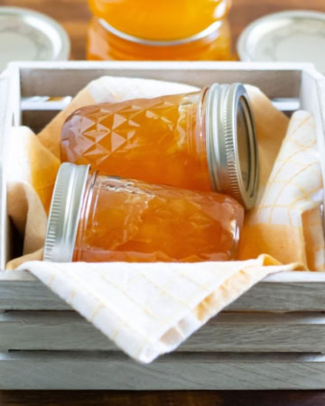 2 jars of homemade peach jam in a wooden crate.