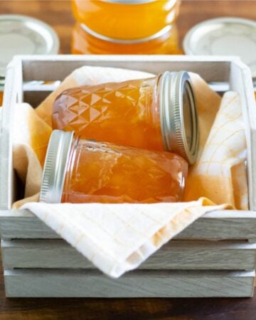 2 jars of homemade peach jam in a wooden crate.