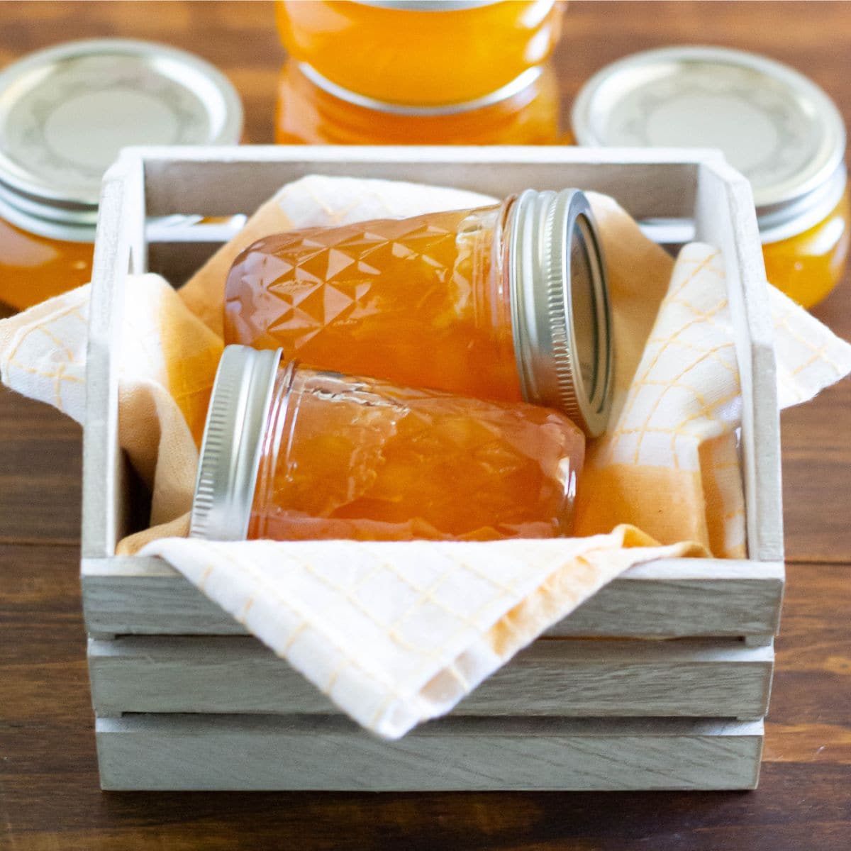 2 jars of homemade peach jam in a wooden crate.