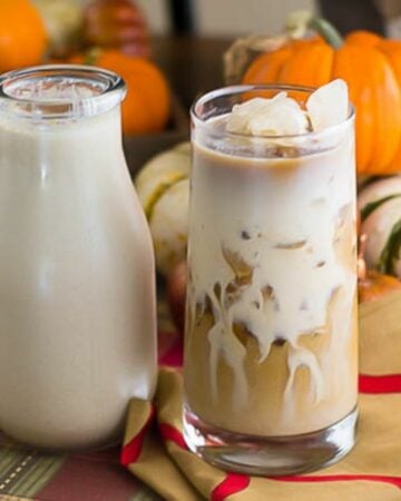 A small bottle of homemade Pumpkin Spice Coffee Creamer next to a glass of iced coffee.