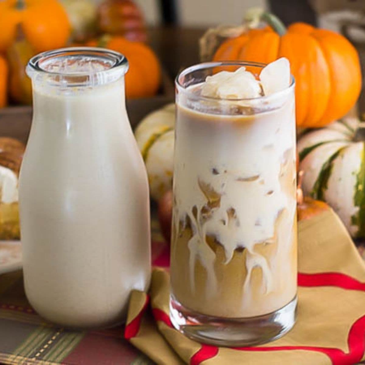 A small bottle of homemade Pumpkin Spice Coffee Creamer next to a glass of iced coffee.