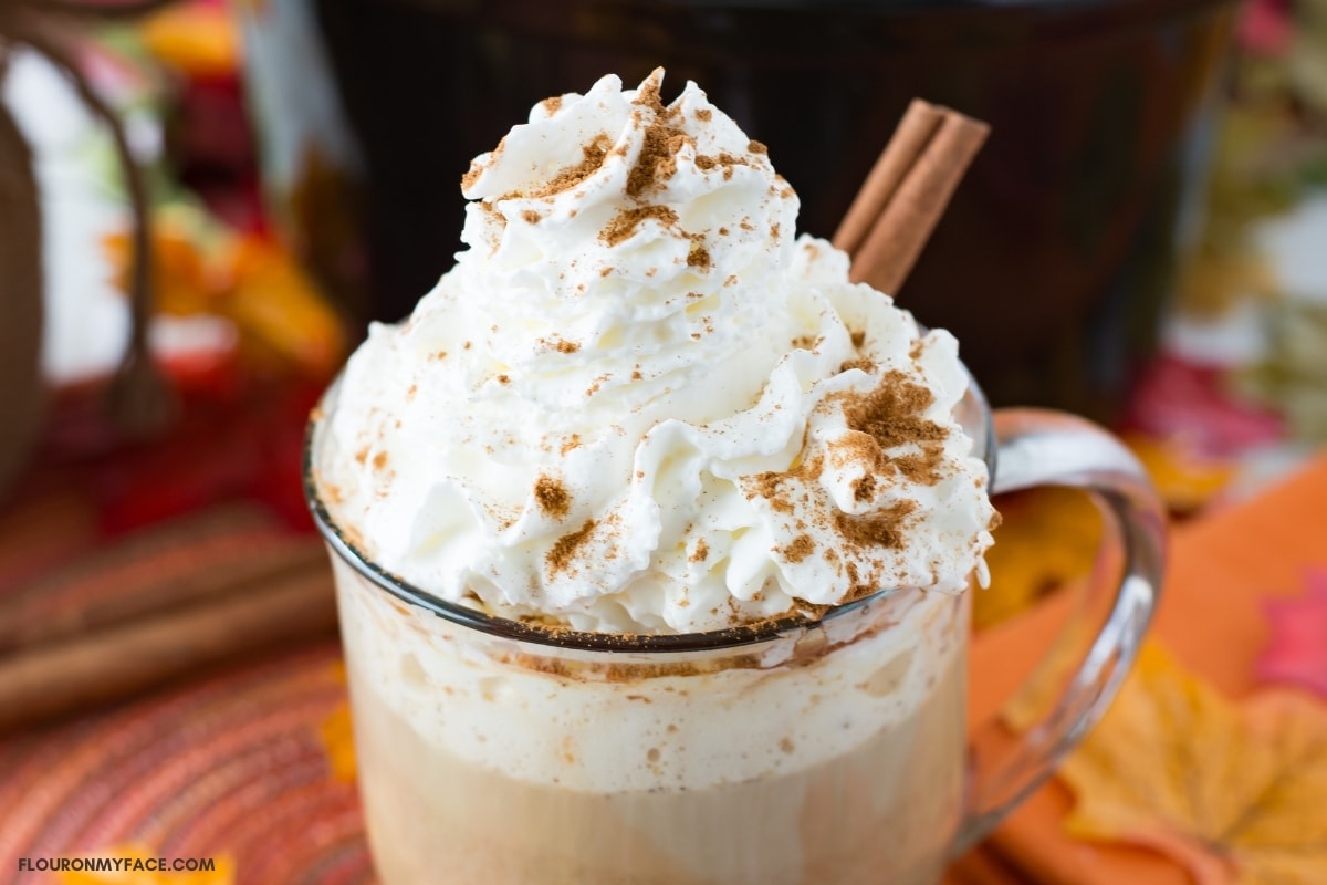 A mug filled with pumpkin spice rumcahatta latter, topped with whipped cream and sprinkled with pumpkin spice seasoning