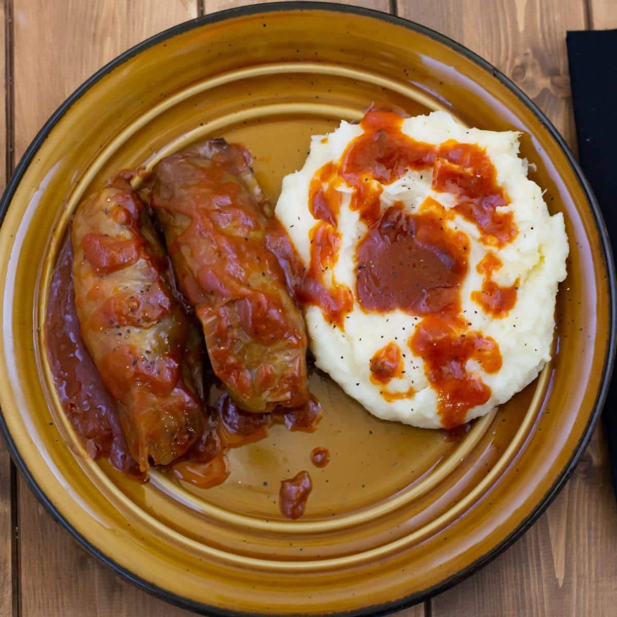 Stuffed cabbage rolls with a tomato based gravy served with mashed potatoes on a dinner plate.