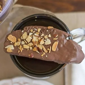 Chocolate dipped biscotti cookie resting on top coffee cup.