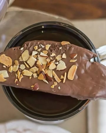 Chocolate dipped biscotti cookie resting on top coffee cup.