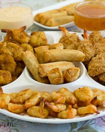 A divided serving dish filled with fried shrimp and spring rolls along with four different dipping sauces.