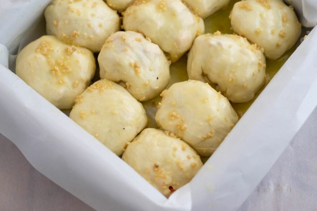 Unbaked pizza bombs brushed with garlic butter in the baking pan.