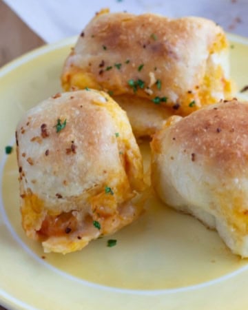 3 homemade pepperoni Pizza Bombs on a plate with a bowl of dipping sauce in the background.