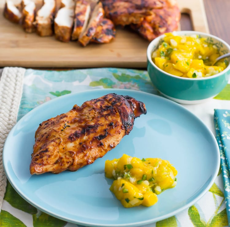 A piece of Pineapple Grilled Chicken on a blue plate with a serving of mango salsa