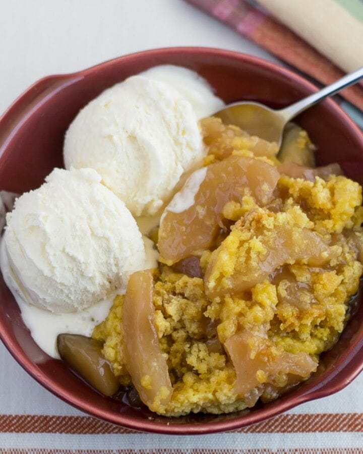 A dessert bowl with caramel apple cake and two scoops of vanilla ice cream.