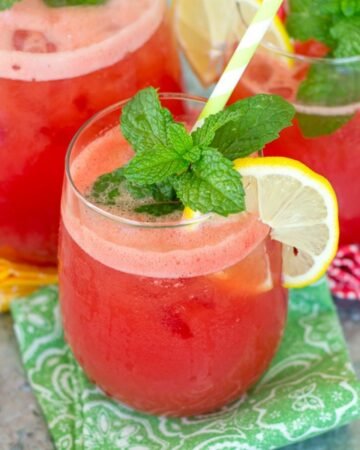 A small glass filled with Watermelon Aqua Fresca with pitcher in background.