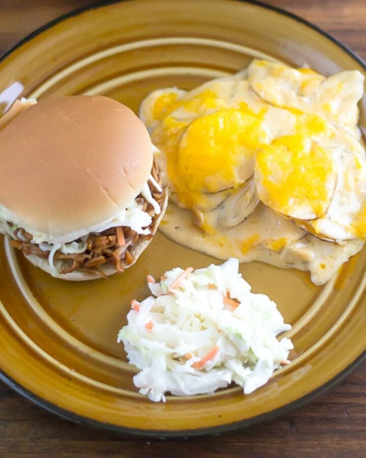 A plate with a serving of scalloped potatoes, a sandwich, and coleslaw.