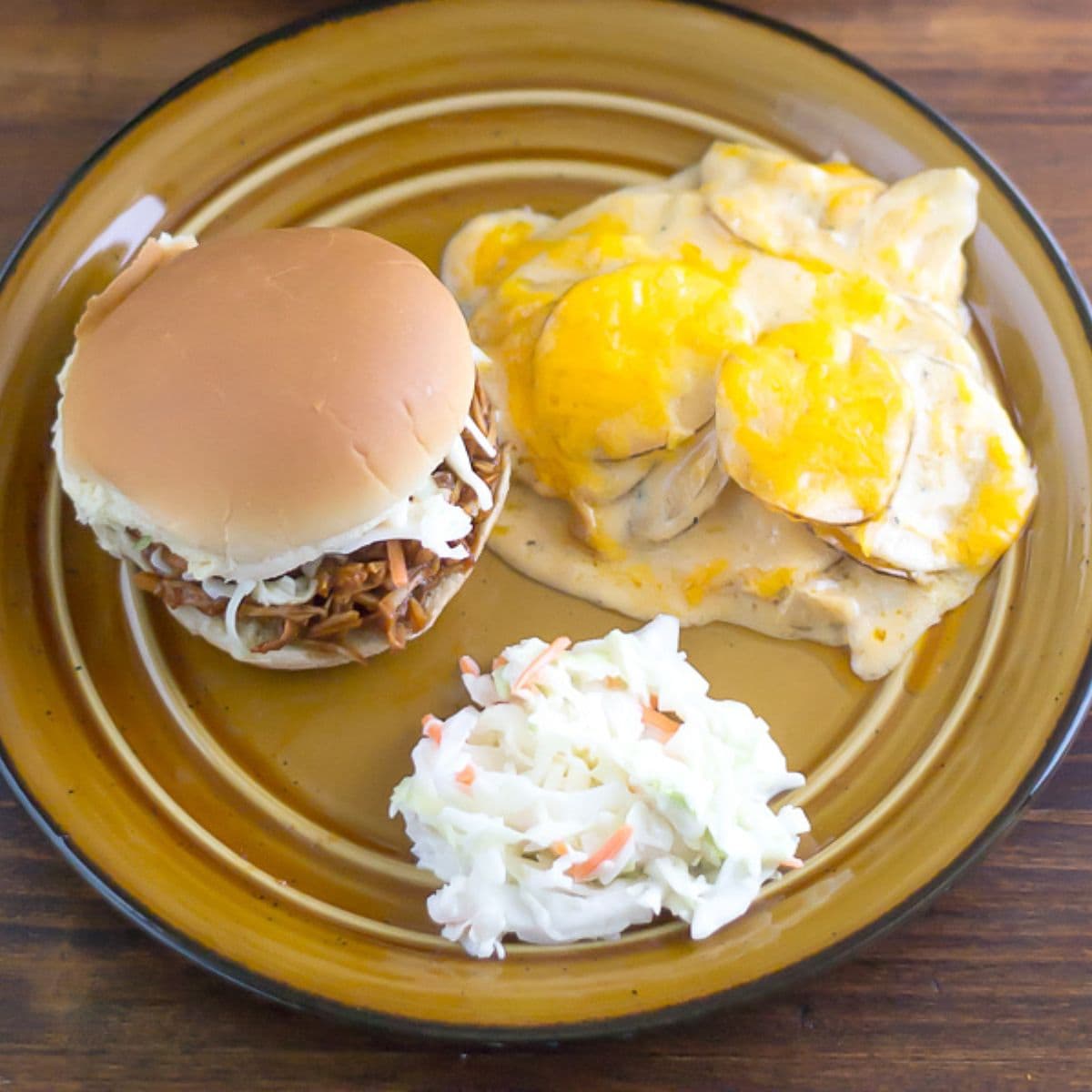 A plate with a serving of scalloped potatoes, a sandwich, and coleslaw.