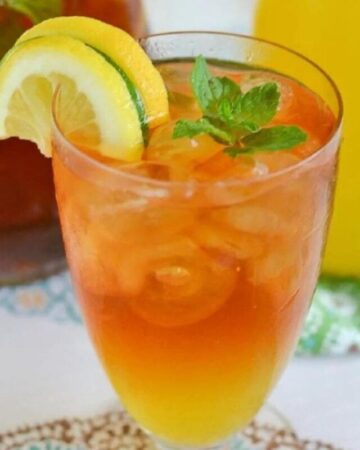 A glass of Mango Iced Tea with lemon and lime wedges and a sprig of mint.