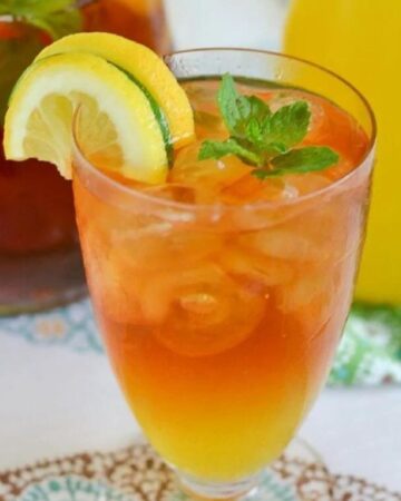 A glass of Mango Iced Tea with lemon and lime wedges and a sprig of mint.