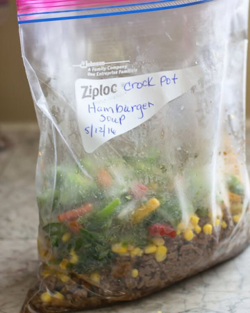 Ingredients for Hamburger soup filling a freezer bag on counter.