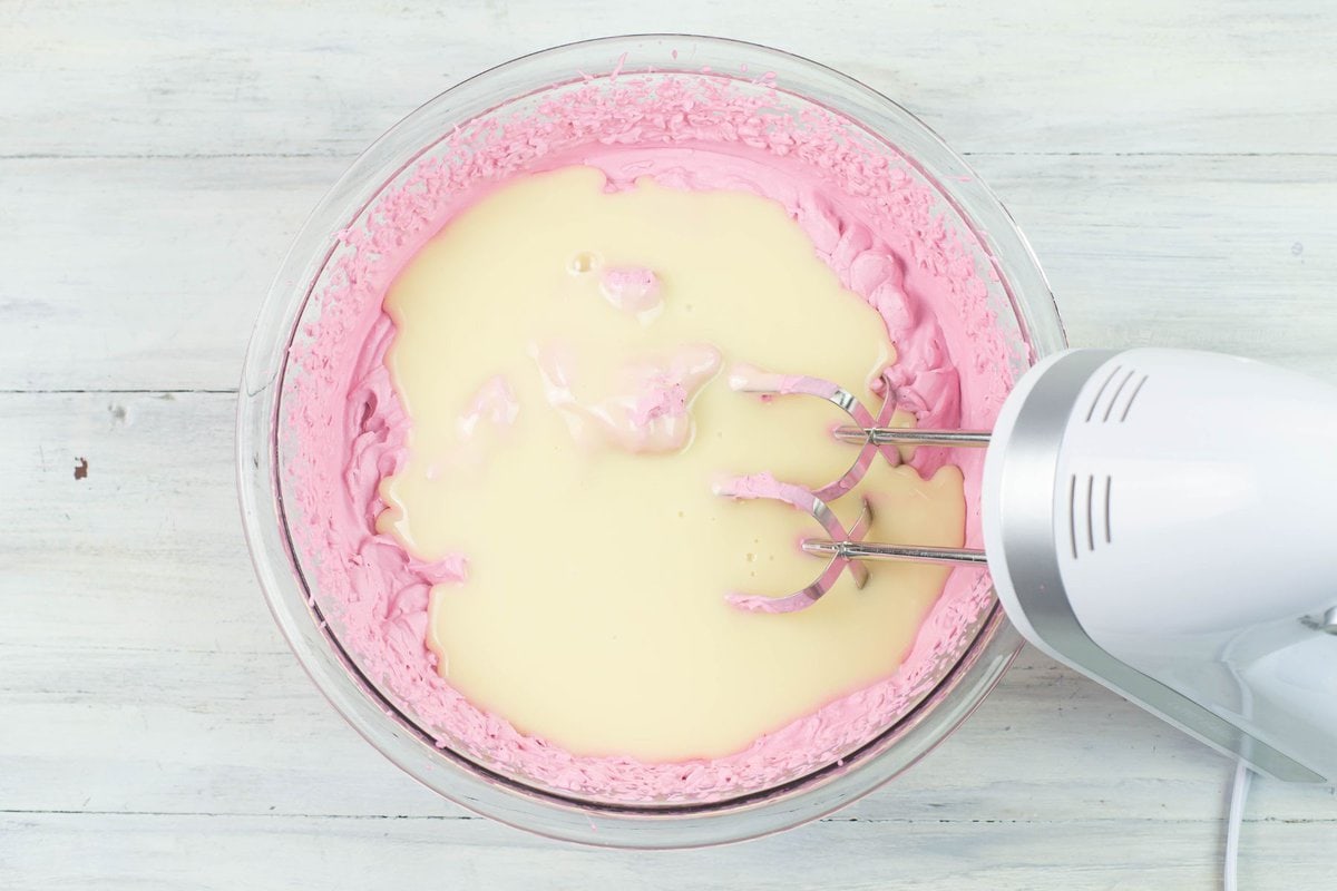 Adding condensed milk to the bowl of ice cream ingredients.