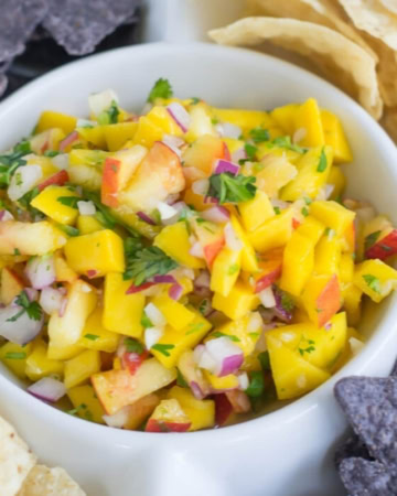 close up photo of mango peach salsa in a dip bowl with white and purple tortilla chips