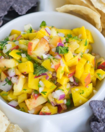 close up photo of mango peach salsa in a dip bowl with white and purple tortilla chips