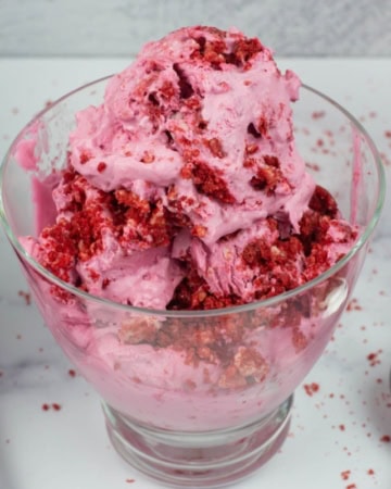 No Churn Red Velvet Cookie Ice Cream in a glass ice cream bowl with a spoon on a pink cloth napkin.