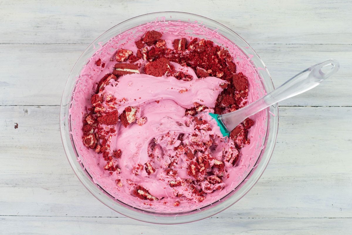 Folding crushed red velvet cookies into ice cream base.