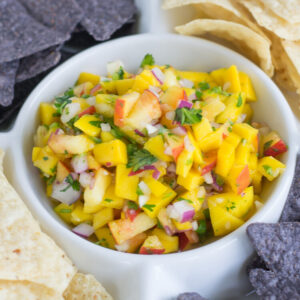 close up photo of mango peach salsa in a dip bowl with white and purple tortilla chips