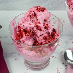 No Churn Red Velvet Cookie Ice Cream in a glass ice cream bowl with a spoon on a pink cloth napkin.