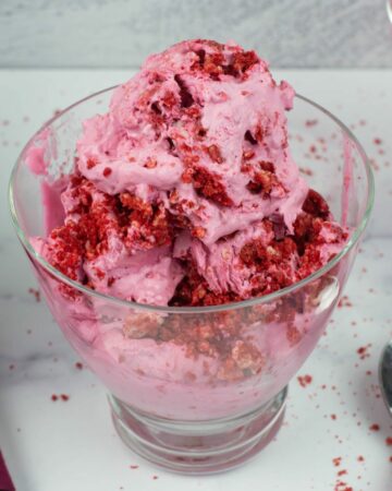 No Churn Red Velvet Cookie Ice Cream in a glass ice cream bowl with a spoon on a pink cloth napkin.
