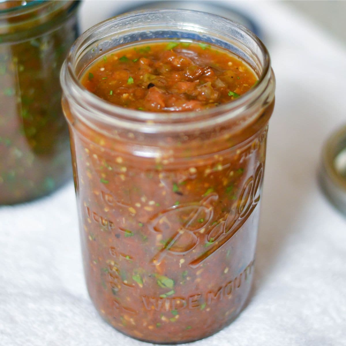 Closeup of a canning jar filled with roasted tomato tomatillo salsa.
