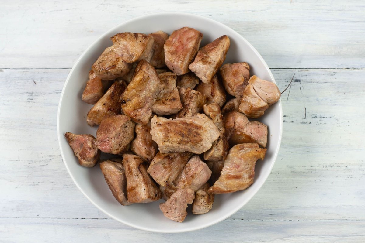 Browned cubed pork pieces in a white glass bowl.