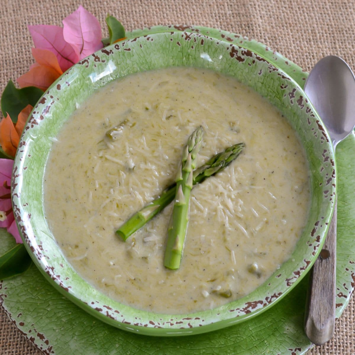 Cream of asparagus soup served in a green bowl with 2 spears of asparagus floating on the soup.