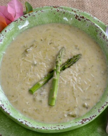 Cream of asparagus soup served in a green bowl with 2 spears of asparagus floating on the soup.