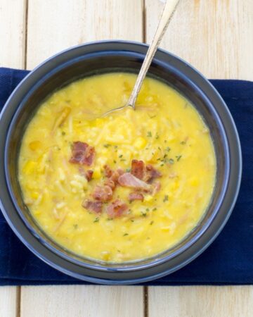 a blue bowl on a blue napkin filled with squash corn chowder with crispy bacon bits on top