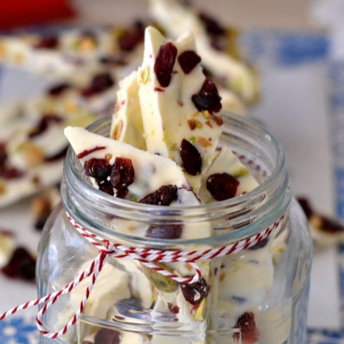 Pieces of cranberry pistachio bark in a glass candy jar peeking out the top.