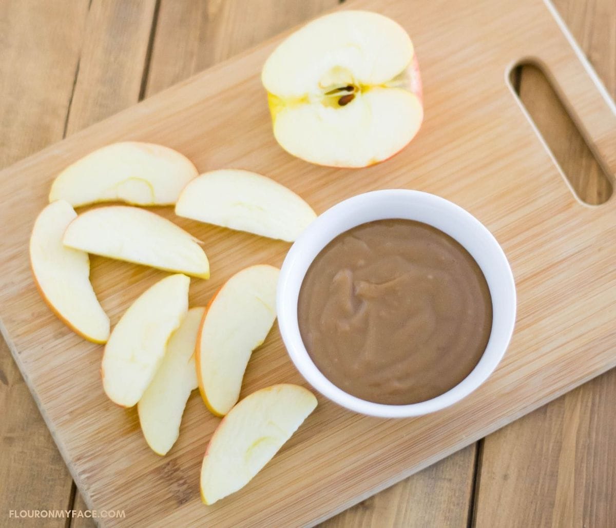 A sliced apple on a cutting board next to a bowl filled with caramel dip.